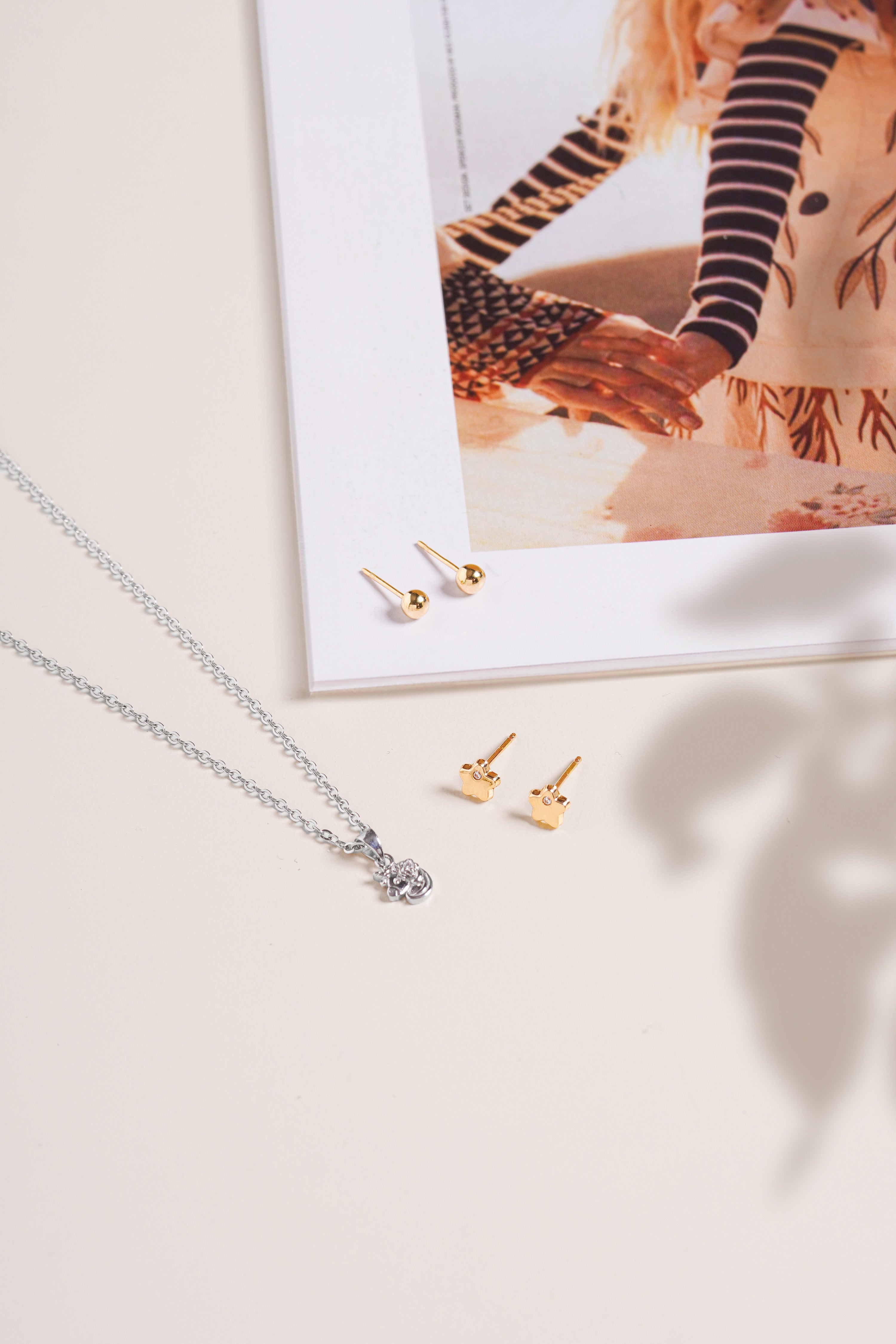 Soho Ball Studs in polished 14K gold shown near a silver necklace on a neutral background with a flat lay composition with magazine.