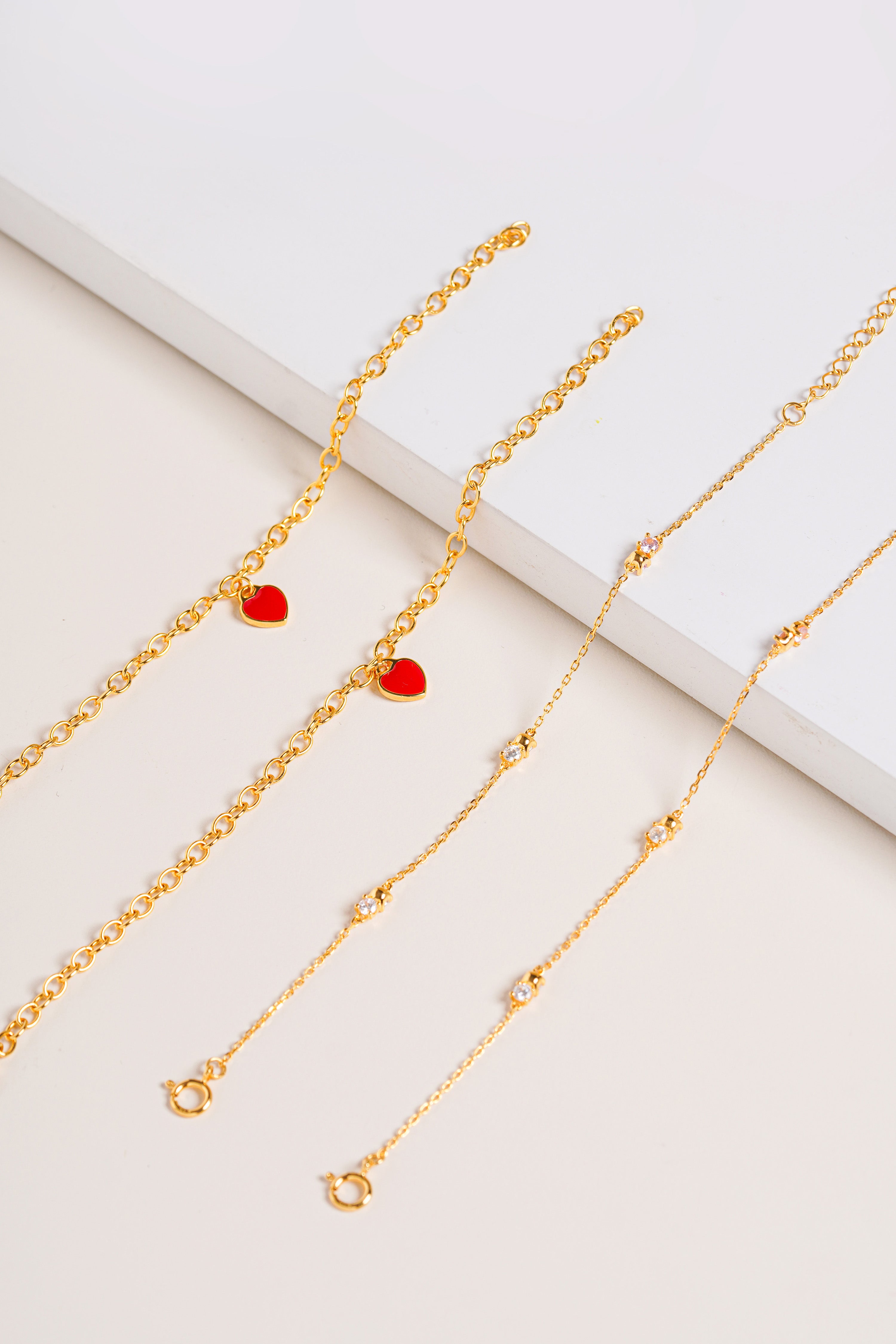 Vermeil chain bracelet with sparkling Cubic Zirconia stones, pictured together with Red Central Heart Bracelet on cream background.