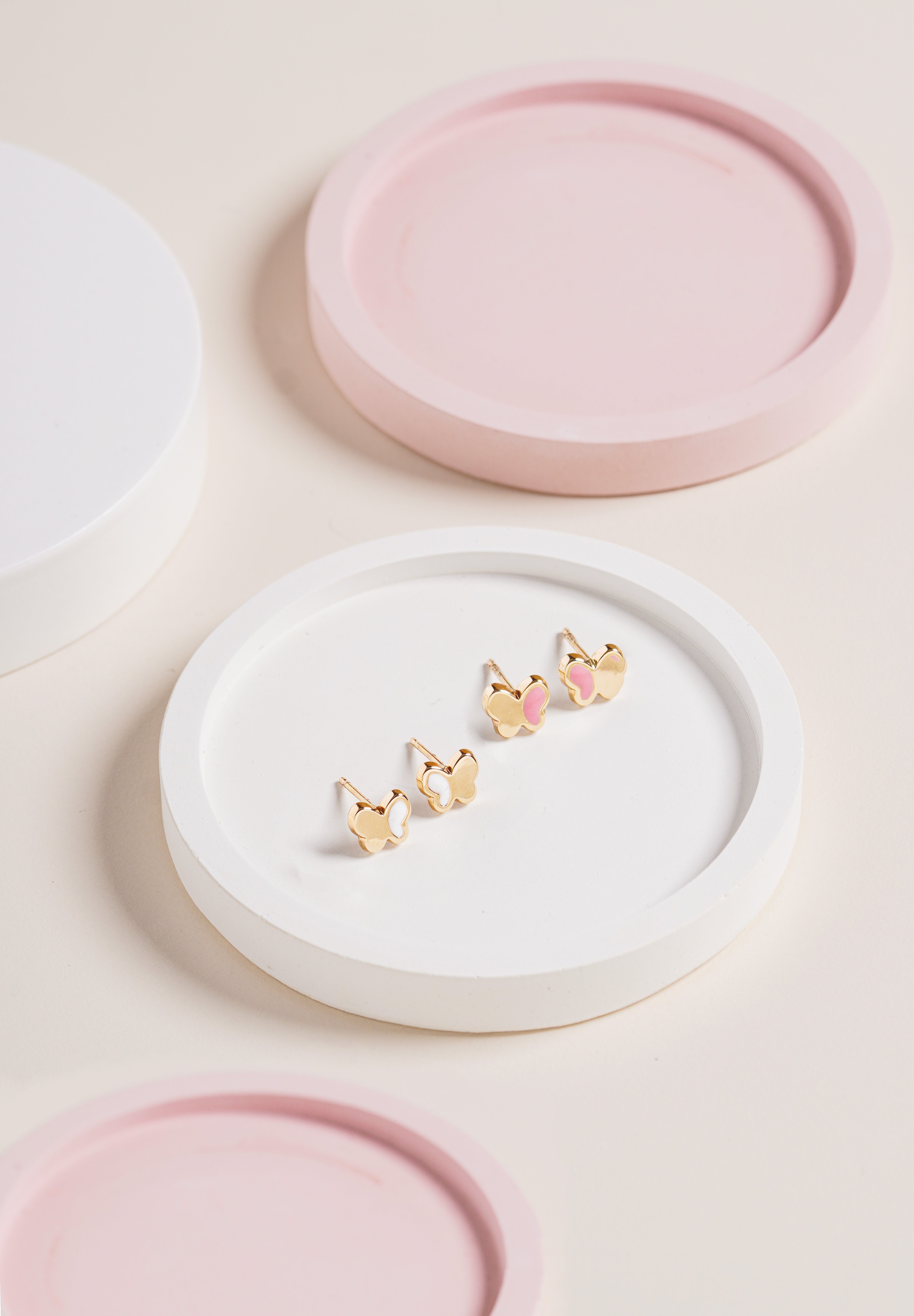 Blue Francis White Hudson Butterfly Studs in 14K gold with white enamel butterfly wings, shown on a white round tray with pastel pink background decor.”