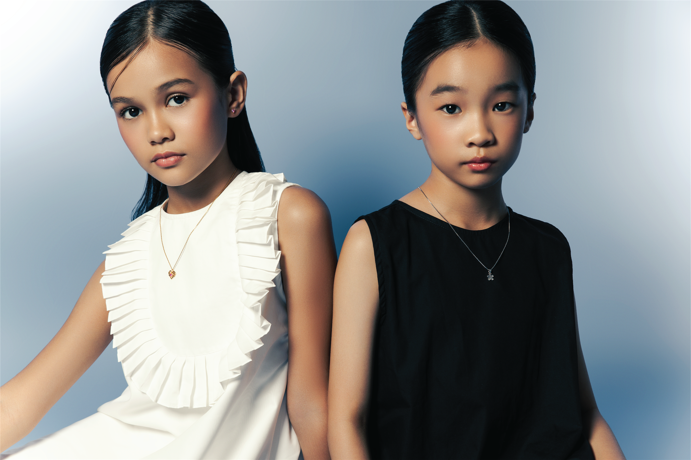 Editorial photo of two models in white and black dresses wearing Blue Francis jewelry, under blue background.