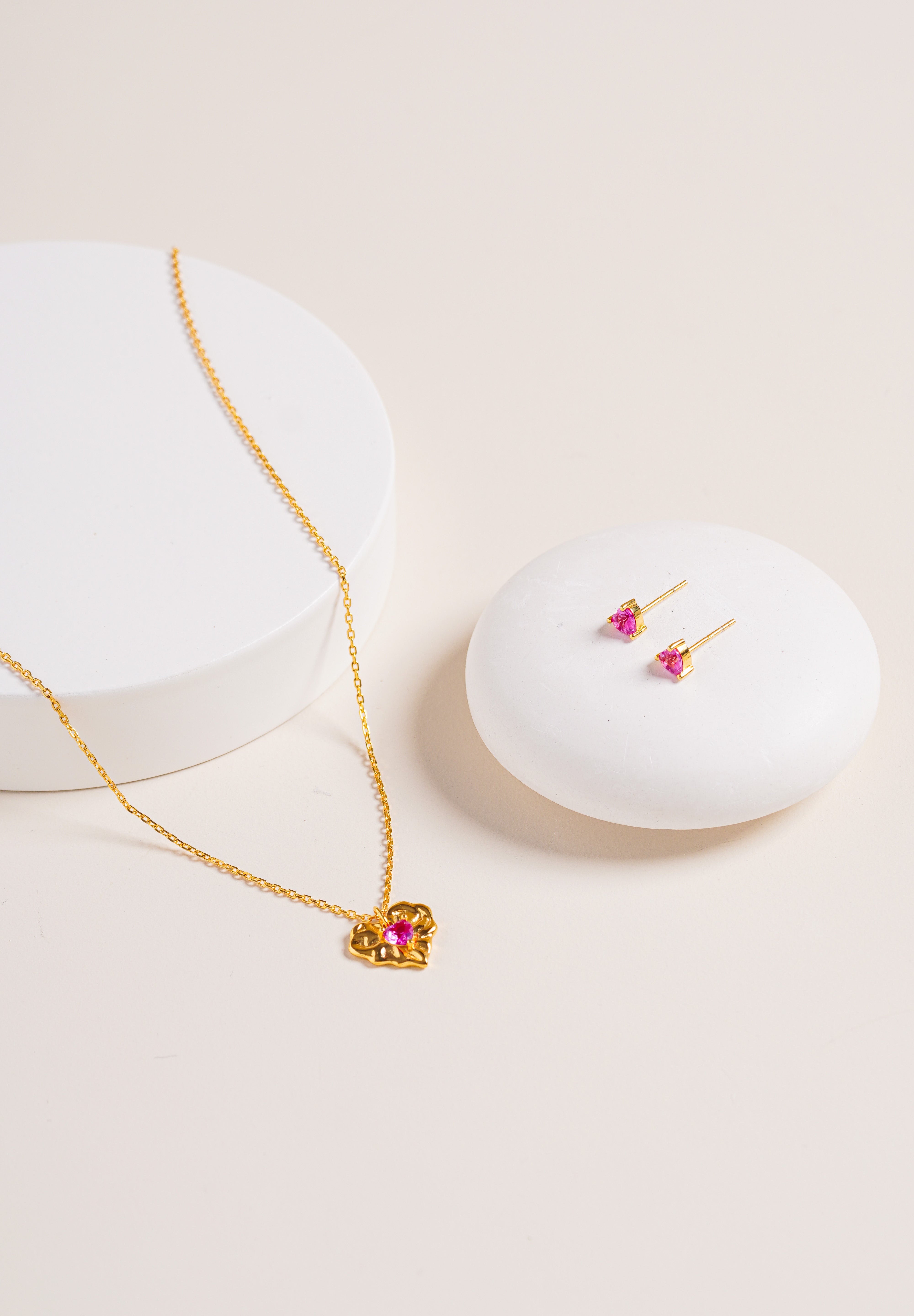 Flat lay of Ruby Liberty Stud Earrings and matching Ruby Liberty Necklace, both in vermeil with ruby corundum stones, on natural background for styling.