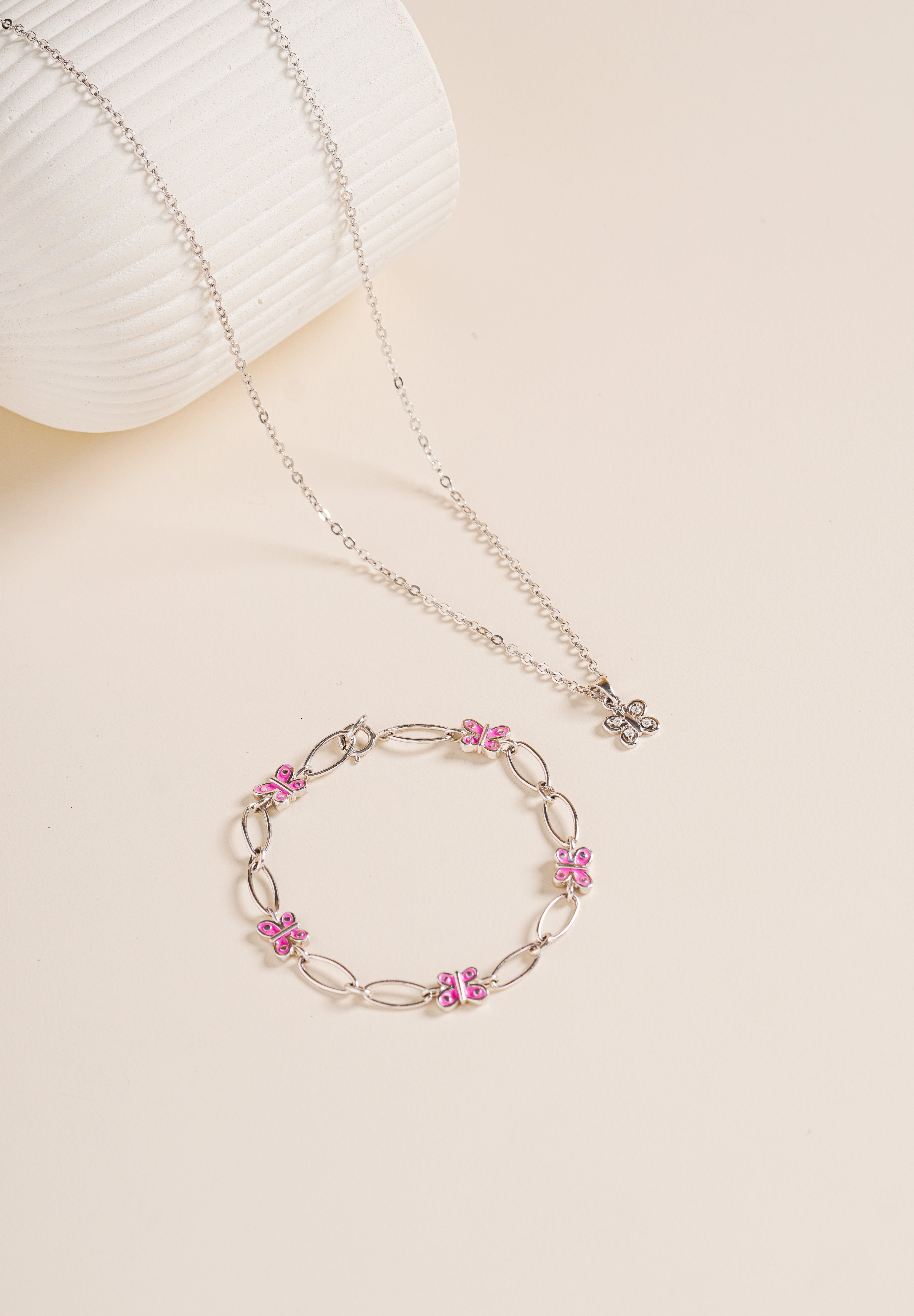 Flat lay of Brooklyn Butterfly Bracelet in pink enamel paired with matching necklace, sterling silver, on neutral background for display.