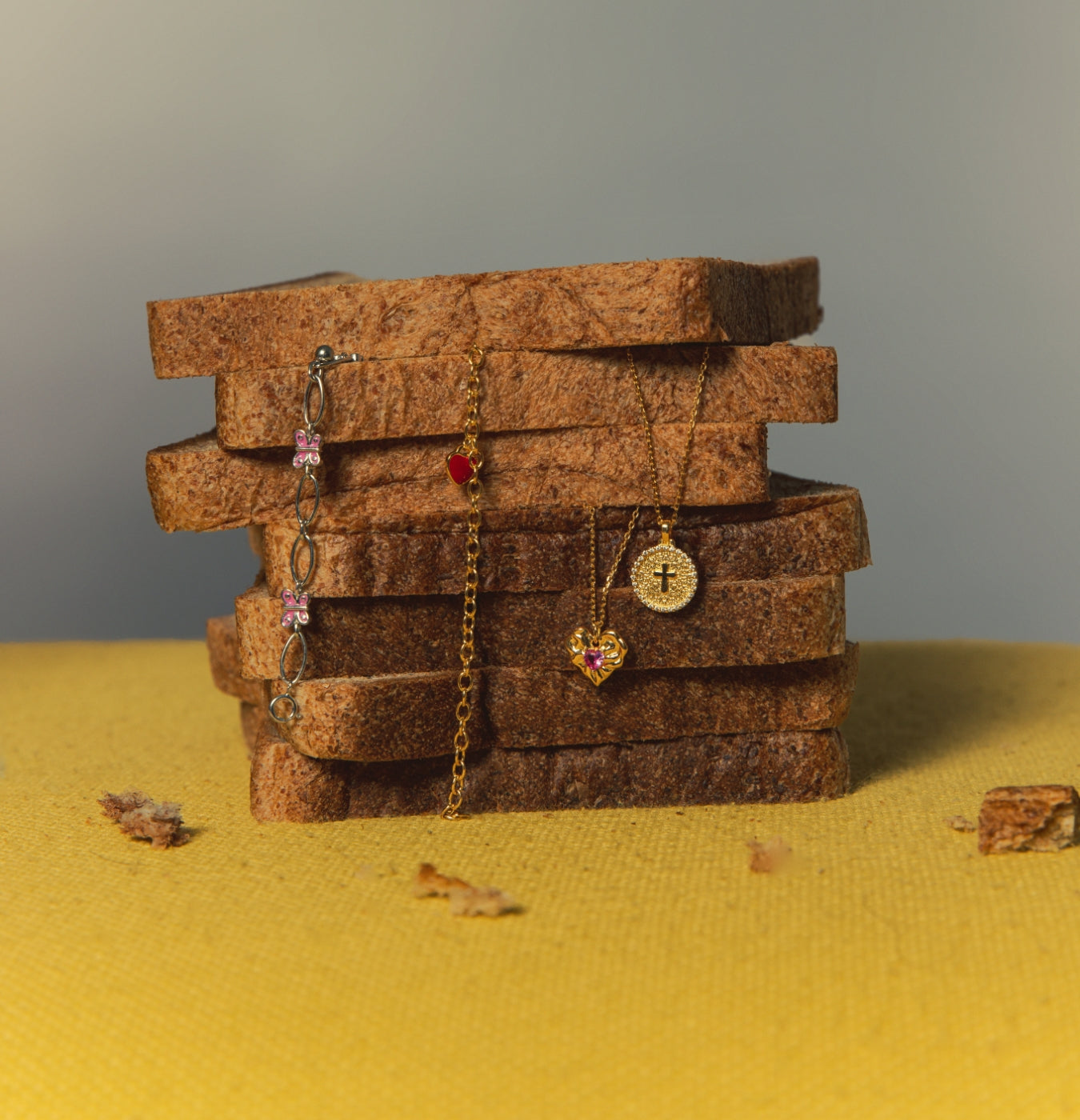 Stack of bread slices with gold and silver jewelry draped across — Bracelet & Necklace Collection, Blue Francis.