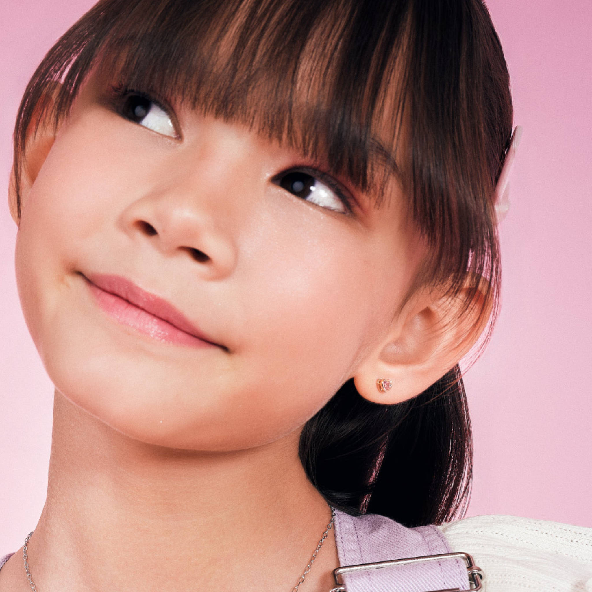 Girl wearing Blue Francis Rosi Twinkle Studs Pink, small 14K gold pink heart screw back earrings sized for kids
