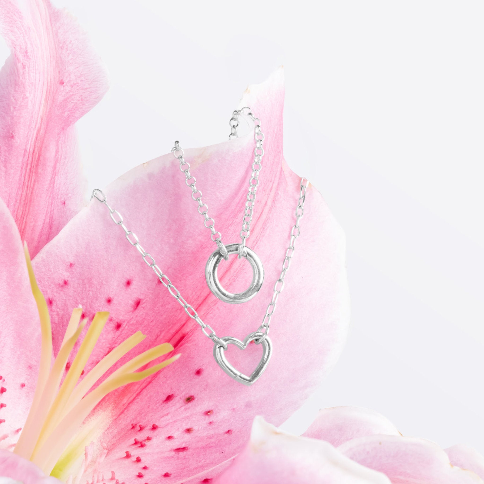 Blue Francis Liam Heart Clasp Necklace and Liam Circle Clasp Necklace in sterling silver on a pink lily
