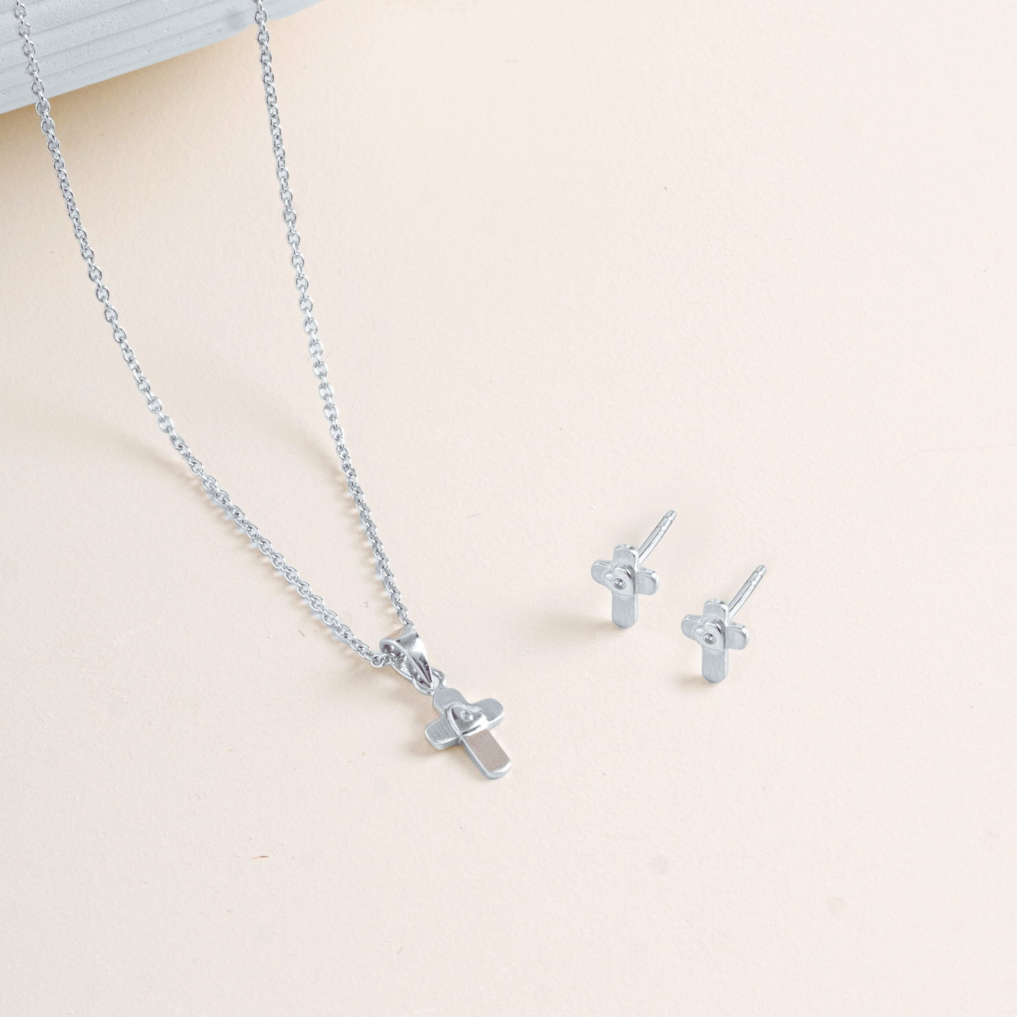 Flat lay picture of Silver cross pendant with cable chain and earrings on a light beige background