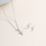 Flat lay picture of Silver cross pendant with cable chain and earrings on a light beige background