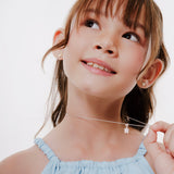 A young girl with brown hair looking up while wearing Brooklyn Butterfly Set. She is wearing a light blue top, and her hand is on the necklace.