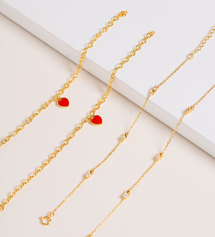 Gold bracelet with red heart pendants enamel and bracelet with Cubic Zirconia stones on a light background
