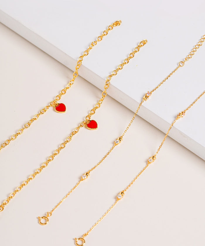 Gold bracelet with red heart pendants enamel and bracelet with Cubic Zirconia stones on a light background