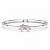 A silver-toned bangle bracelet featuring a small floral cluster centerpiece with pink stones and clear round stones, shown on a plain white background.