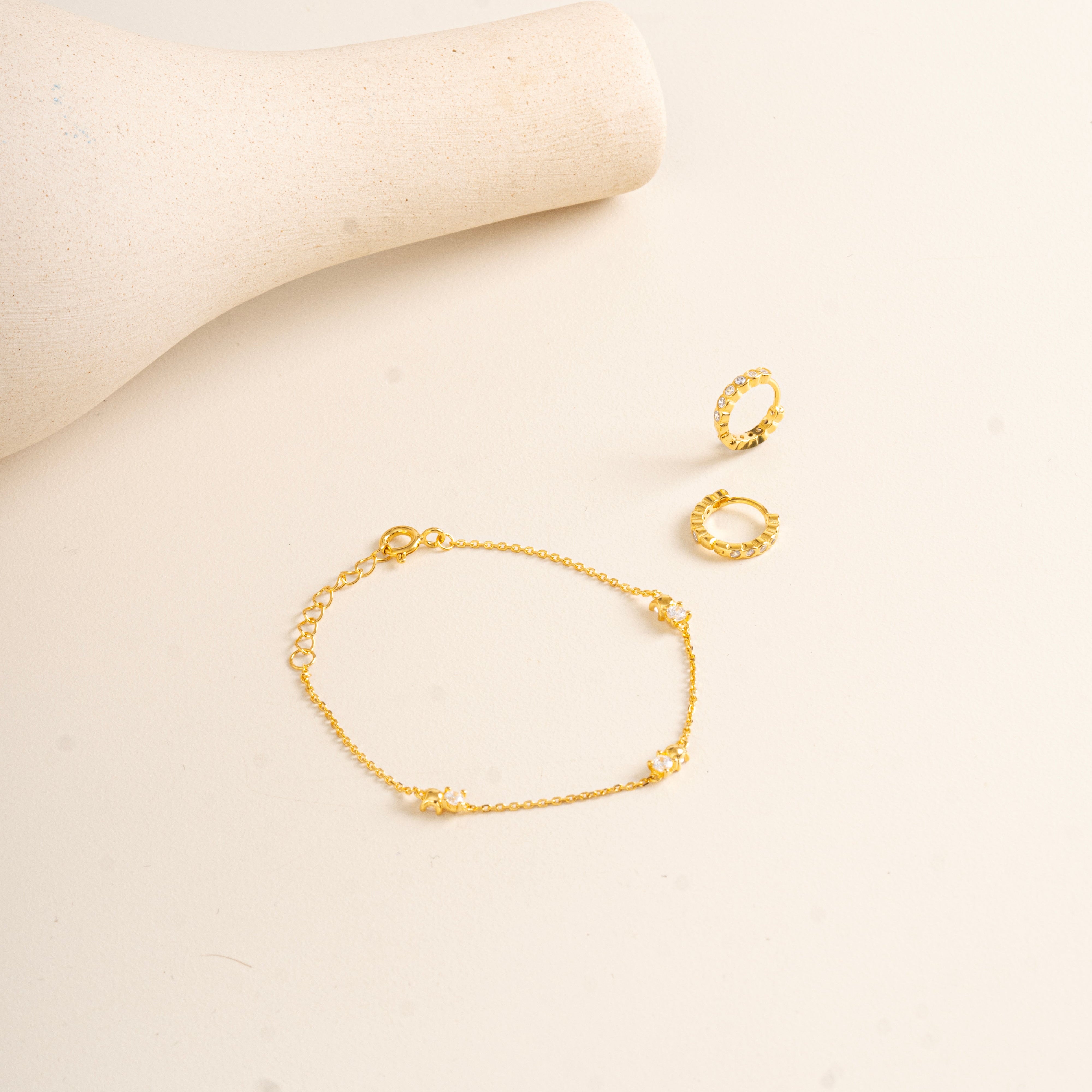 Gold Vermeil Twinkle bracelet and gold vermeil Twinkle hoops on a beige background
