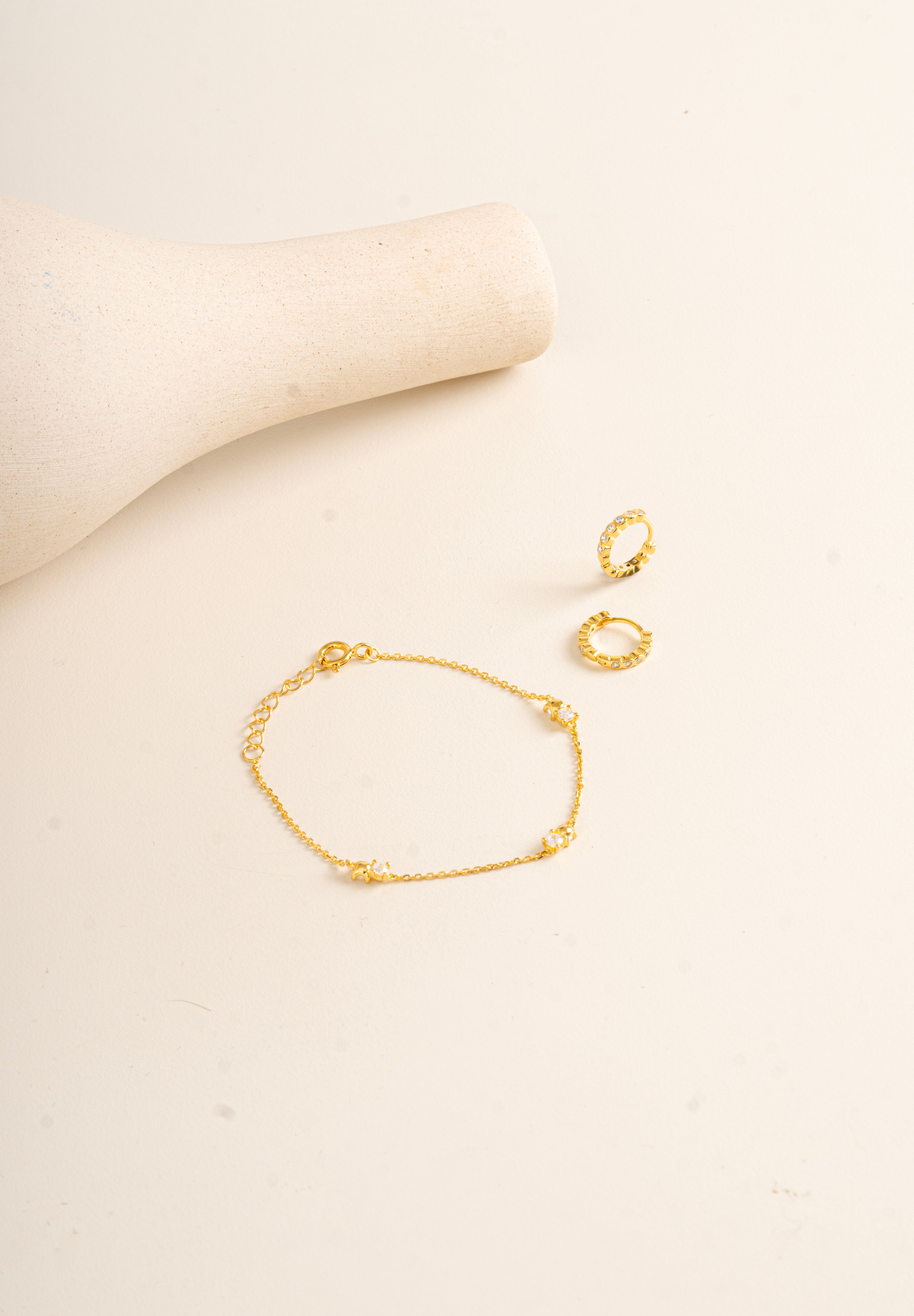 Gold Vermeil Twinkle bracelet and gold vermeil Twinkle hoops on a beige background