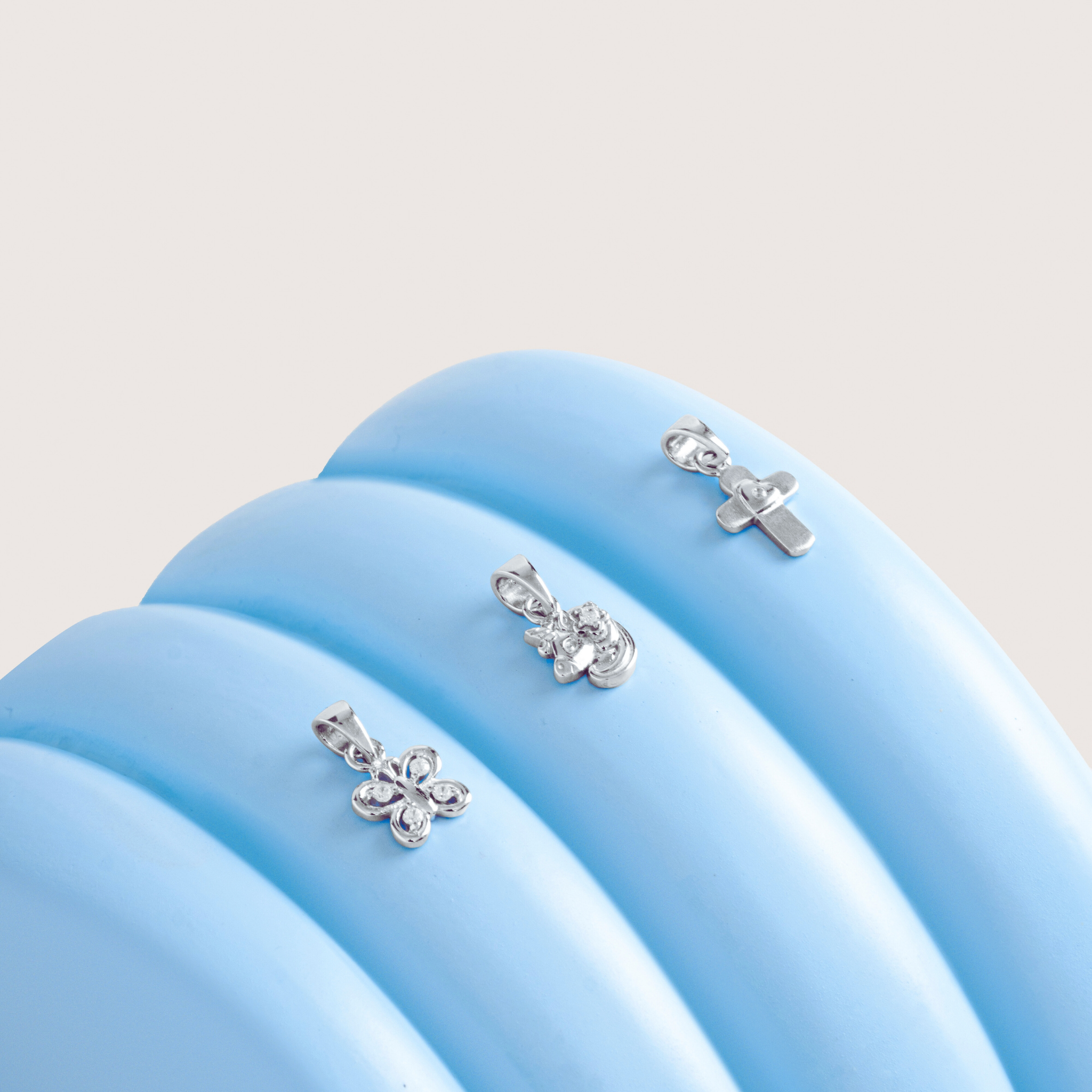 Silver butterfly, unicorn and cross pendants on a blue cushion with a light cream background