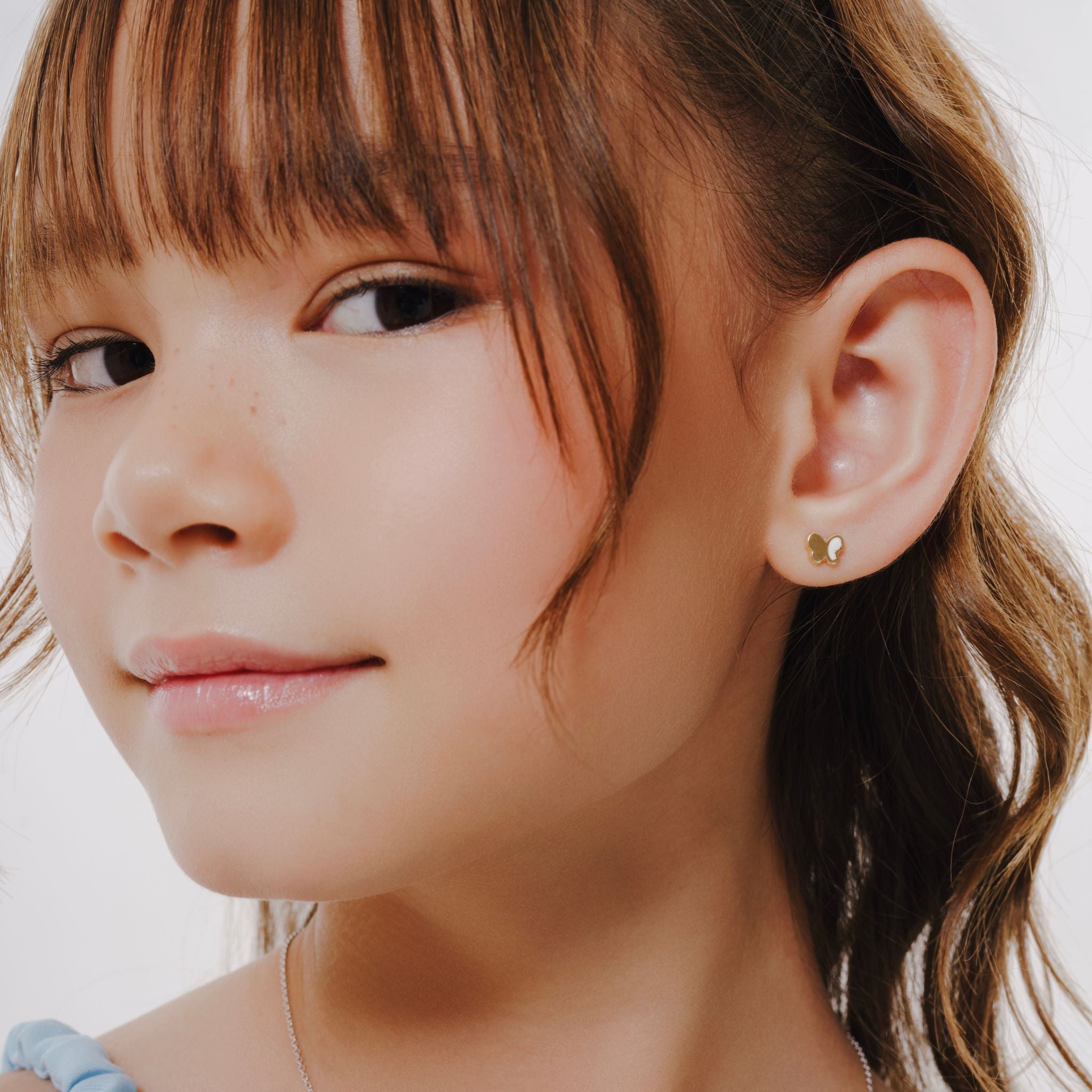 Blue Francis Kids Earrings in Gold 14K White Hudson Butterfly Studs. In the picture is a close-up of blue francis model wearing a small earring with a neutral background.