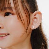 Blue Francis Kids Stud Earrings in Sterling Silver, Brooklyn Cross Earrings. A close-up picture of a person wearing a small cross silver sterling earring with a neutral background.