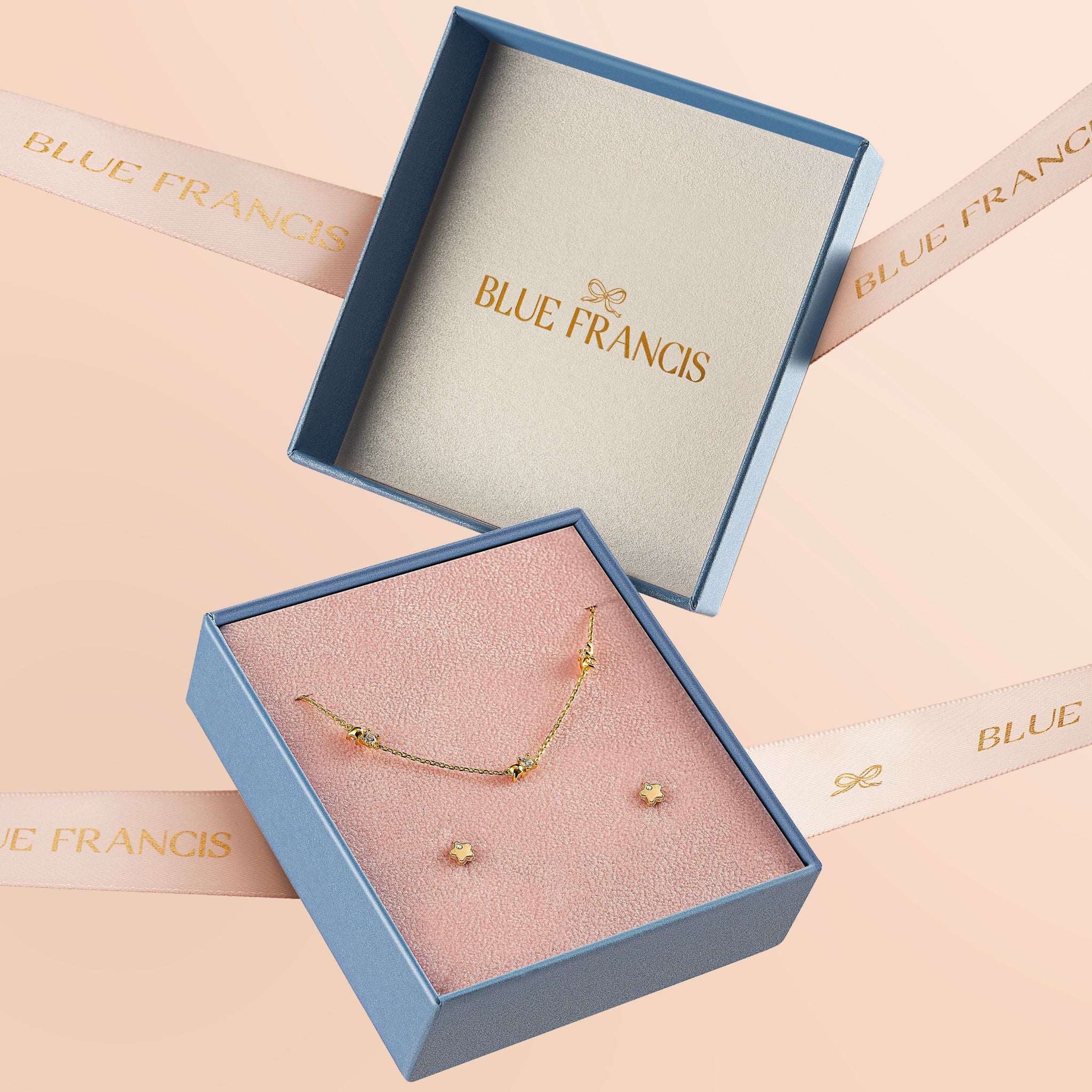 Gold necklace and earrings in a Blue Francis box on a beige background, a sample of Blue Francis Packaging for Butter Cream Hudson Butterfly Earrings.