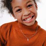 Blue Francis teens Brooklyn Cross Pendant in Sterling Silver. Blue Francis model wearing an orange sweater with a white background, wearing Brooklyn Cross Pendant and 1mm Box chain in Sterling Silver.