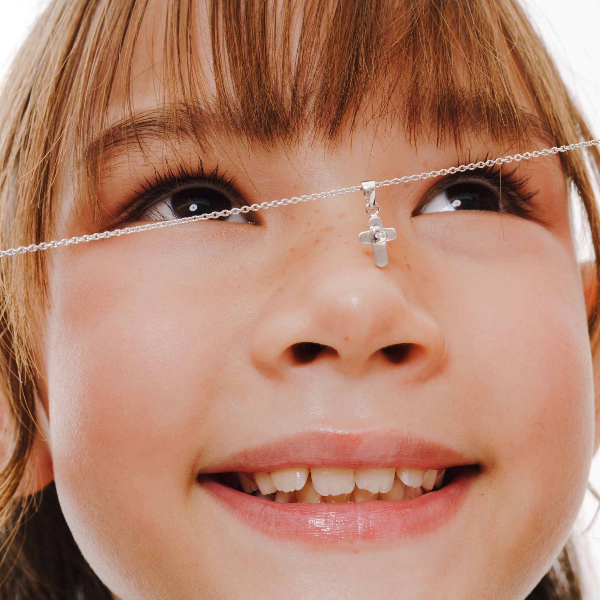 Blue Francis - Tweens Chain in Sterling Silver and a Brooklyn cross pendant on Cable Chain. This is a close-up picture of a child's face with a necklace featuring a cross pendant and chain cable. 