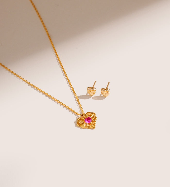 Gold necklace and earrings with a pink gemstone on a beige background