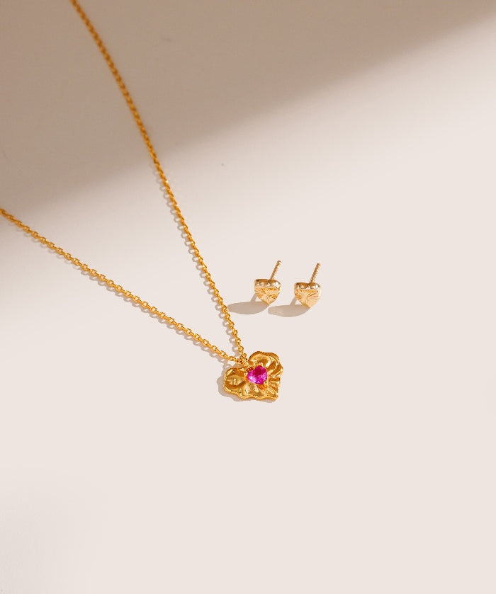 Gold necklace and earrings with a pink gemstone on a beige background