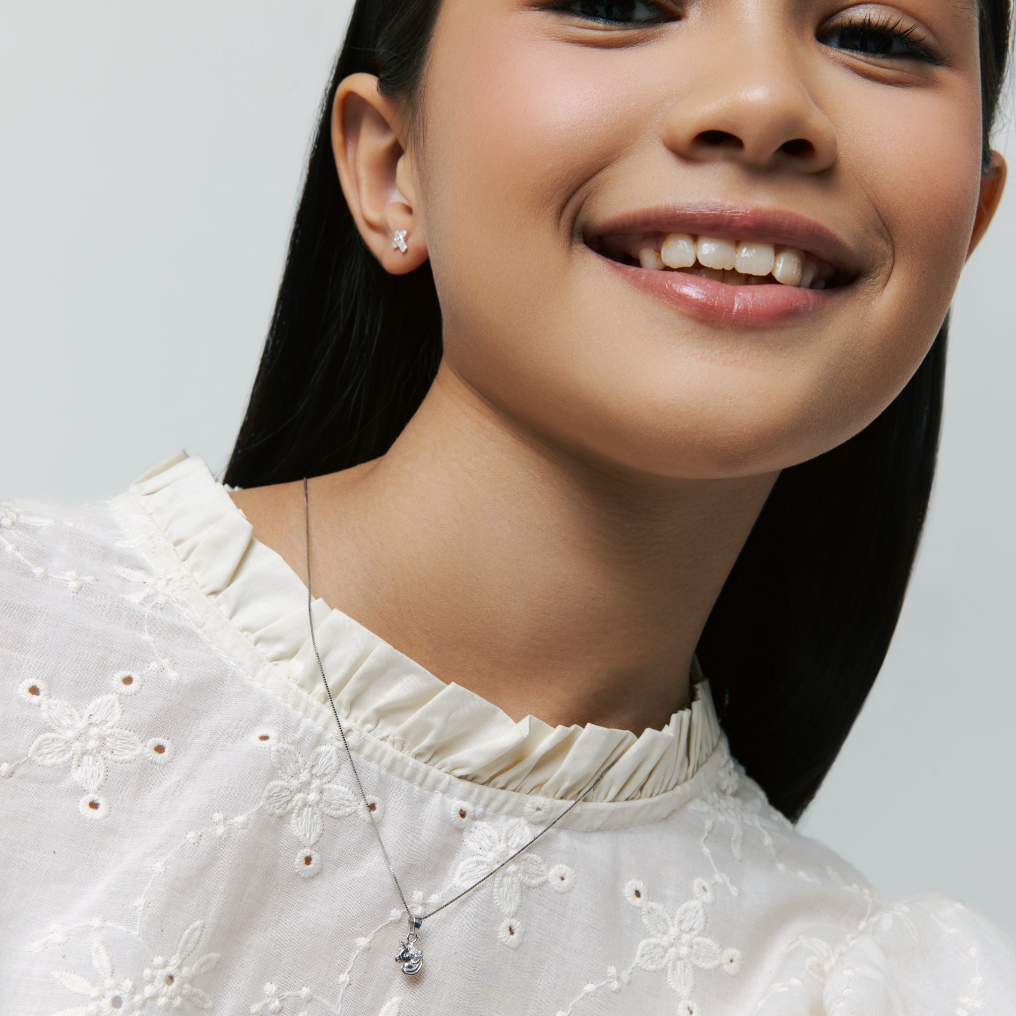 Model wears Brooklyn Unicorn Necklace with box chain not sold separately and Brooklyn Cross Stud Earrings, in sterling silver, smiling on neutral background.