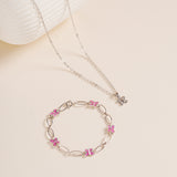 Flat lay of Brooklyn Butterfly Necklace in sterling silver with cubic zirconia stone beside pink enamel Butterfly Bracelet on neutral background for styling.