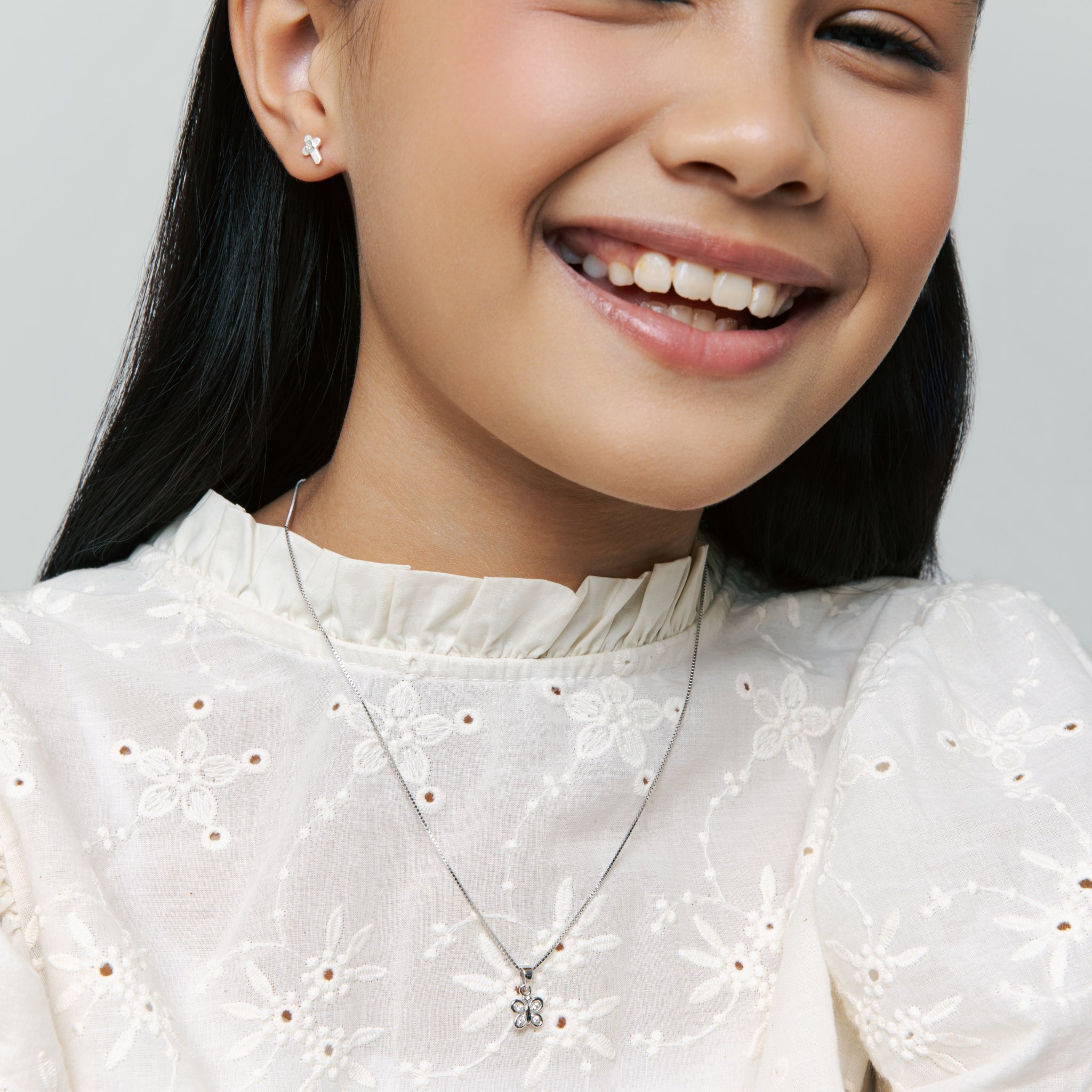 Model wears Brooklyn Butterfly Necklace in sterling silver with cubic zirconia stone and Brooklyn Cross Stud Earrings, smiling on neutral background.