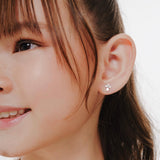 Blue Francis Kids Stud Earrings in Sterling Silver, Brooklyn Cross Earrings. A close-up picture of a person wearing a small cross silver sterling earring with a neutral background.