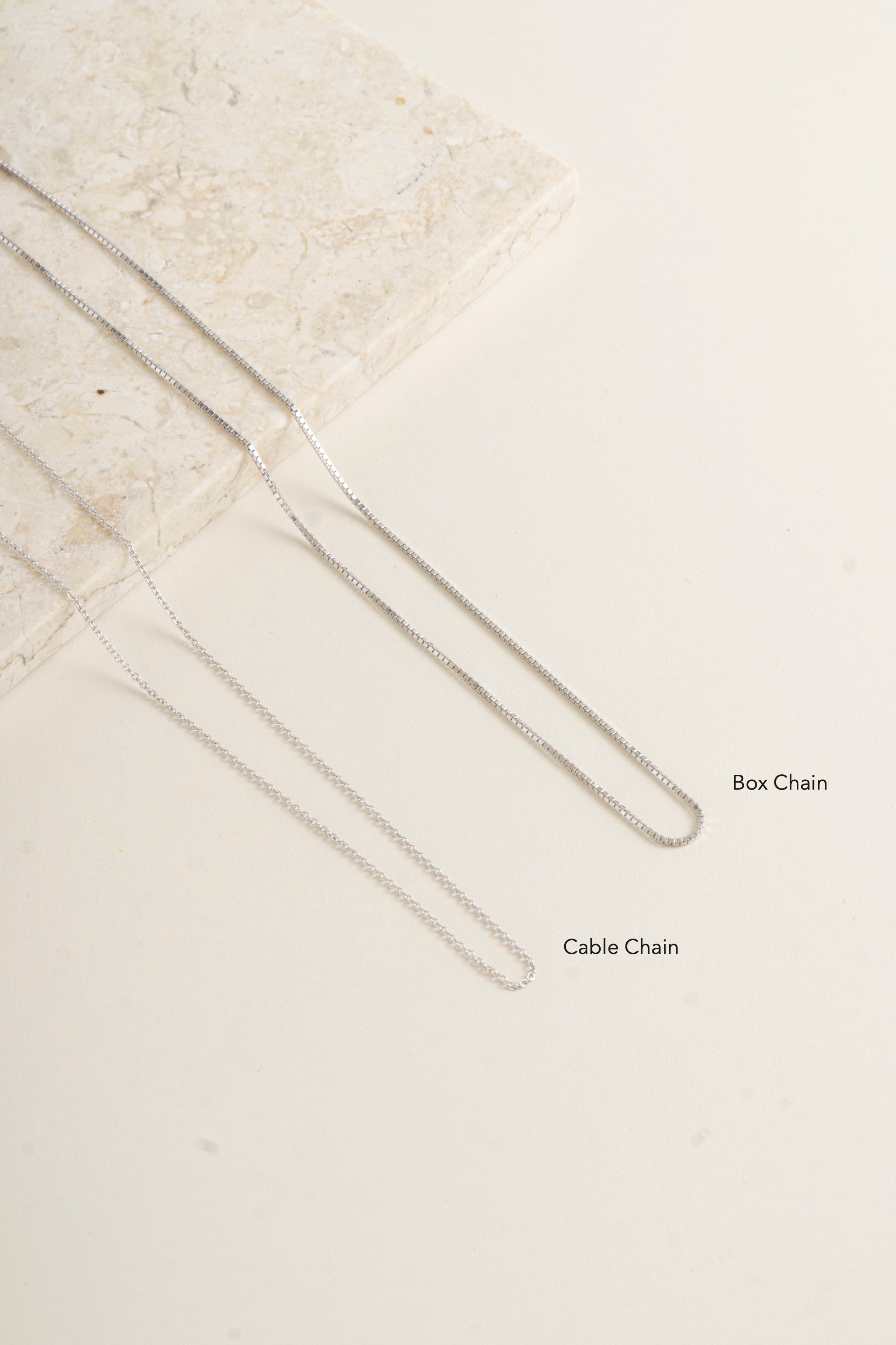 Close-up of box chain and cable chain on a textured beige surface - Blue Francis