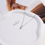 Brooklyn Cross Necklace in sterling silver shown draped on a white ceramic dish next to cross stud earrings, styled with a fashion magazine.