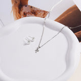 Brooklyn Cross Necklace in sterling silver shown draped on a white ceramic dish next to cross stud earrings, styled with a fashion magazine.