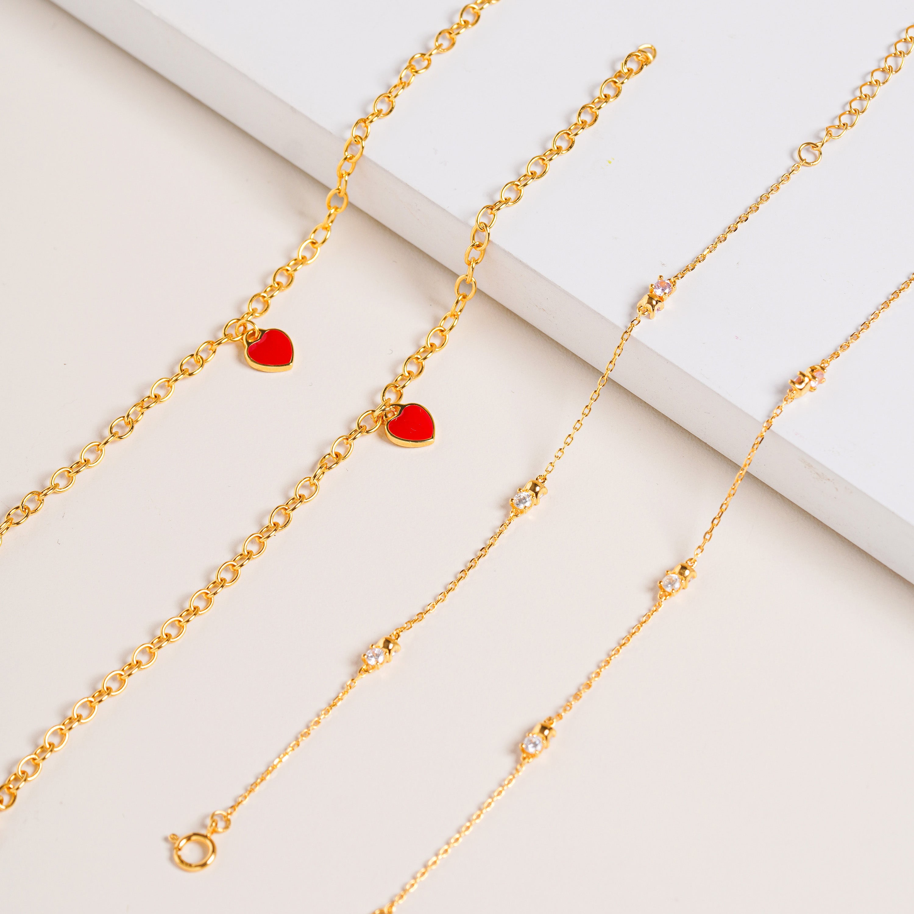 Red Central Heart Bracelet in gold vermeil featuring a gold rolo chain with small red heart charms, displayed on a cream background.
