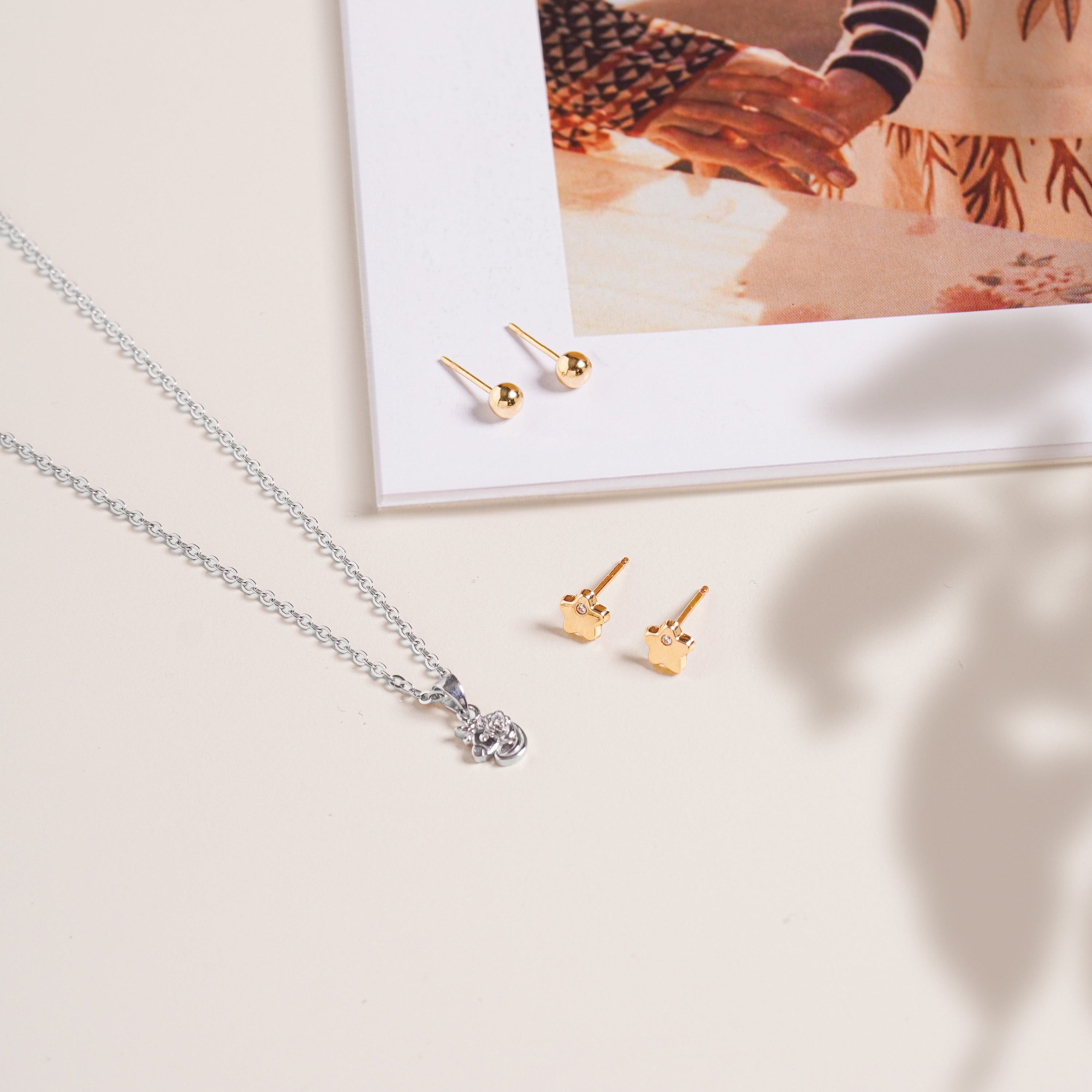 Soho Ball Studs in polished 14K gold shown near a silver necklace on a neutral background with a flat lay composition with magazine.