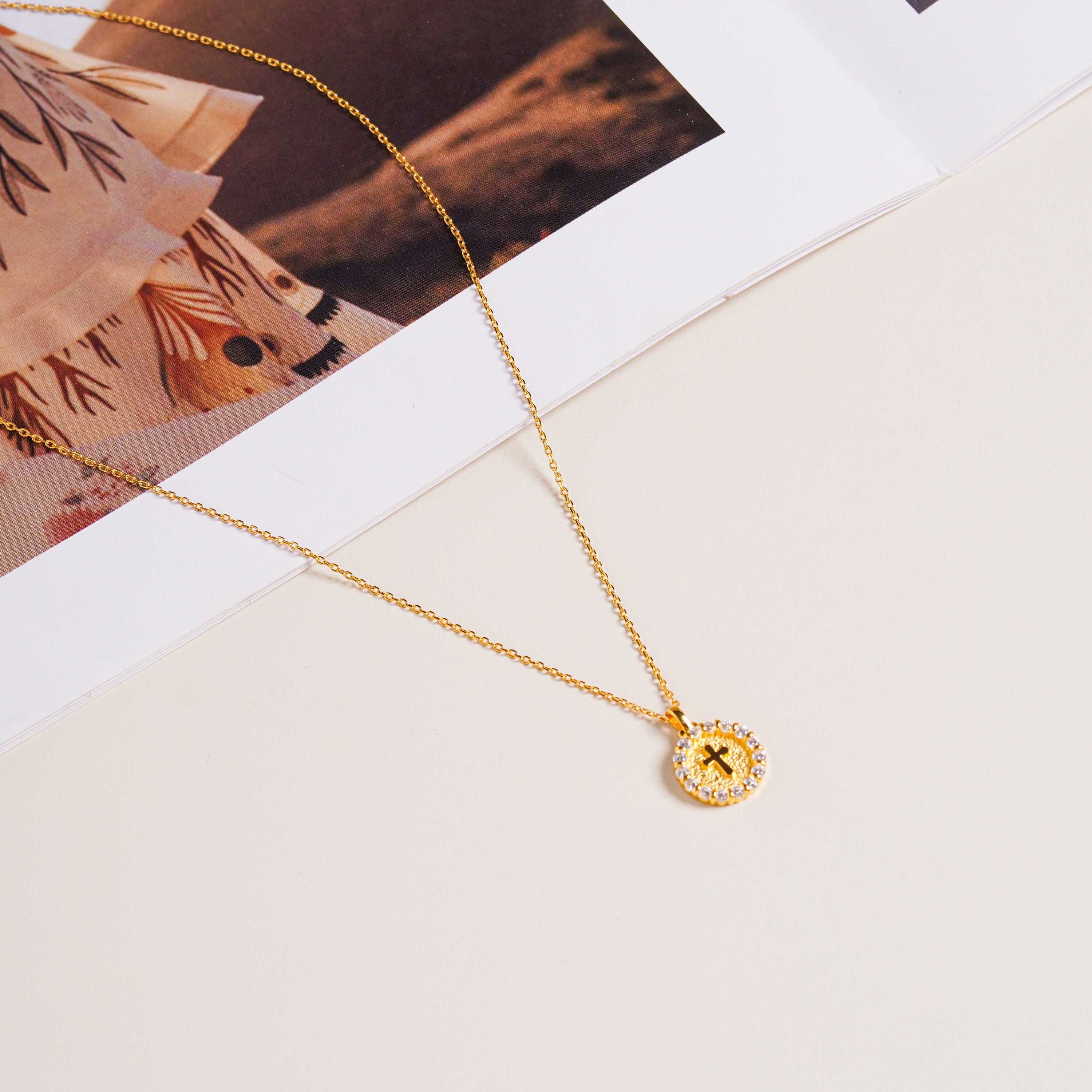 Gold vermeil Twinkle Cross Necklace with sparkling round pendant on a cream background.