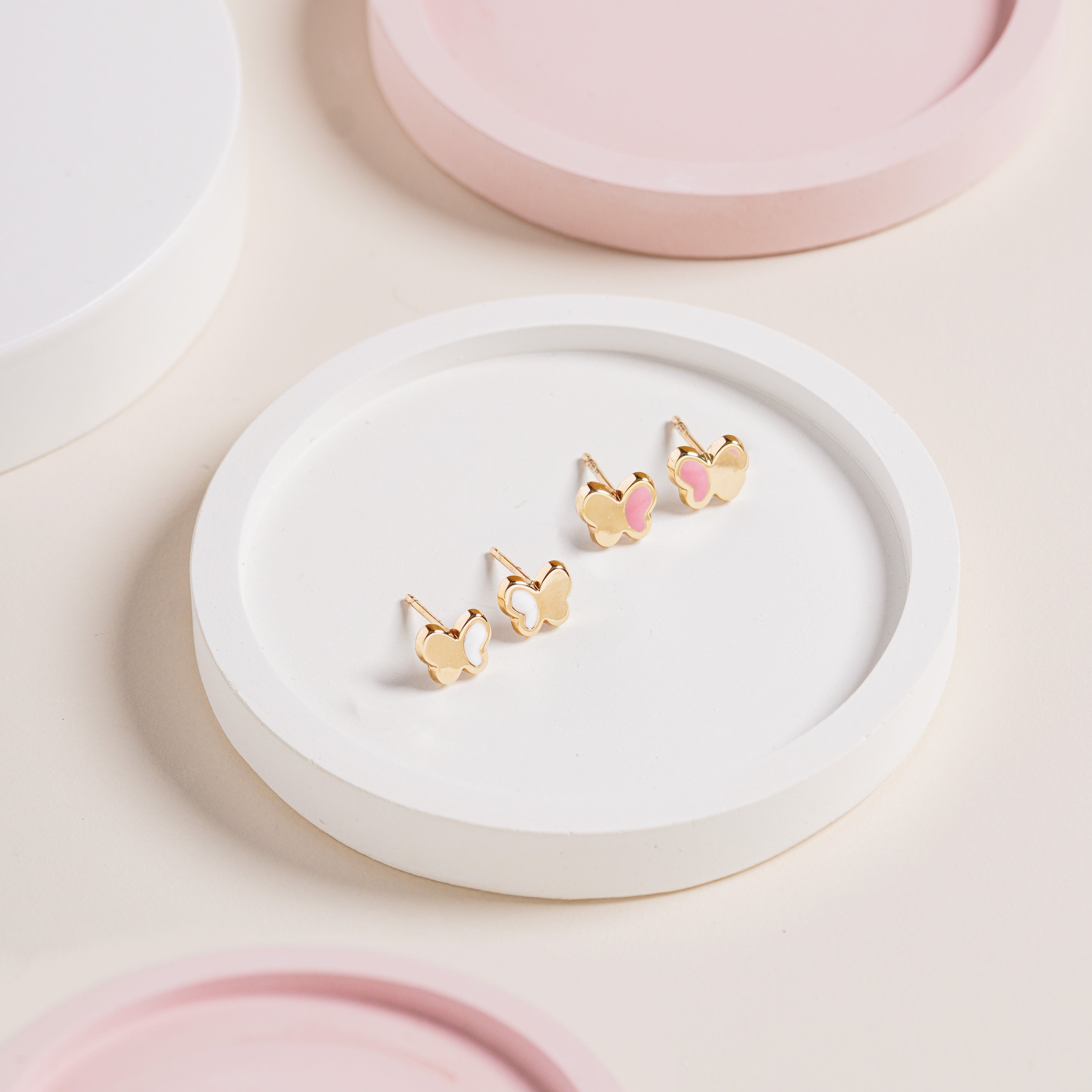Blue Francis White Hudson Butterfly Studs in 14K gold with white enamel butterfly wings, shown on a white round tray with pastel pink background decor.”