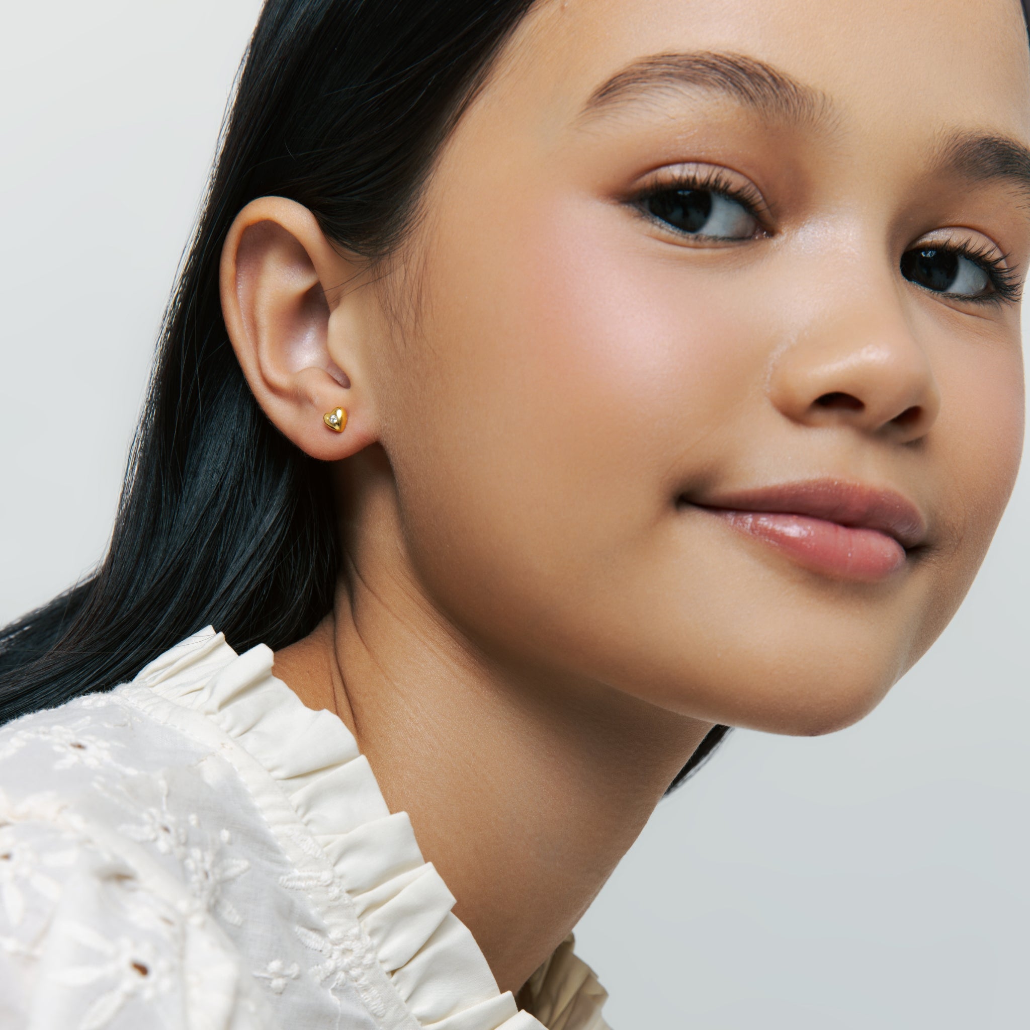 Model wearing Blue Francis gold heart stud earring with cubic zirconia stone, featured for the Homepage Earring Tab.