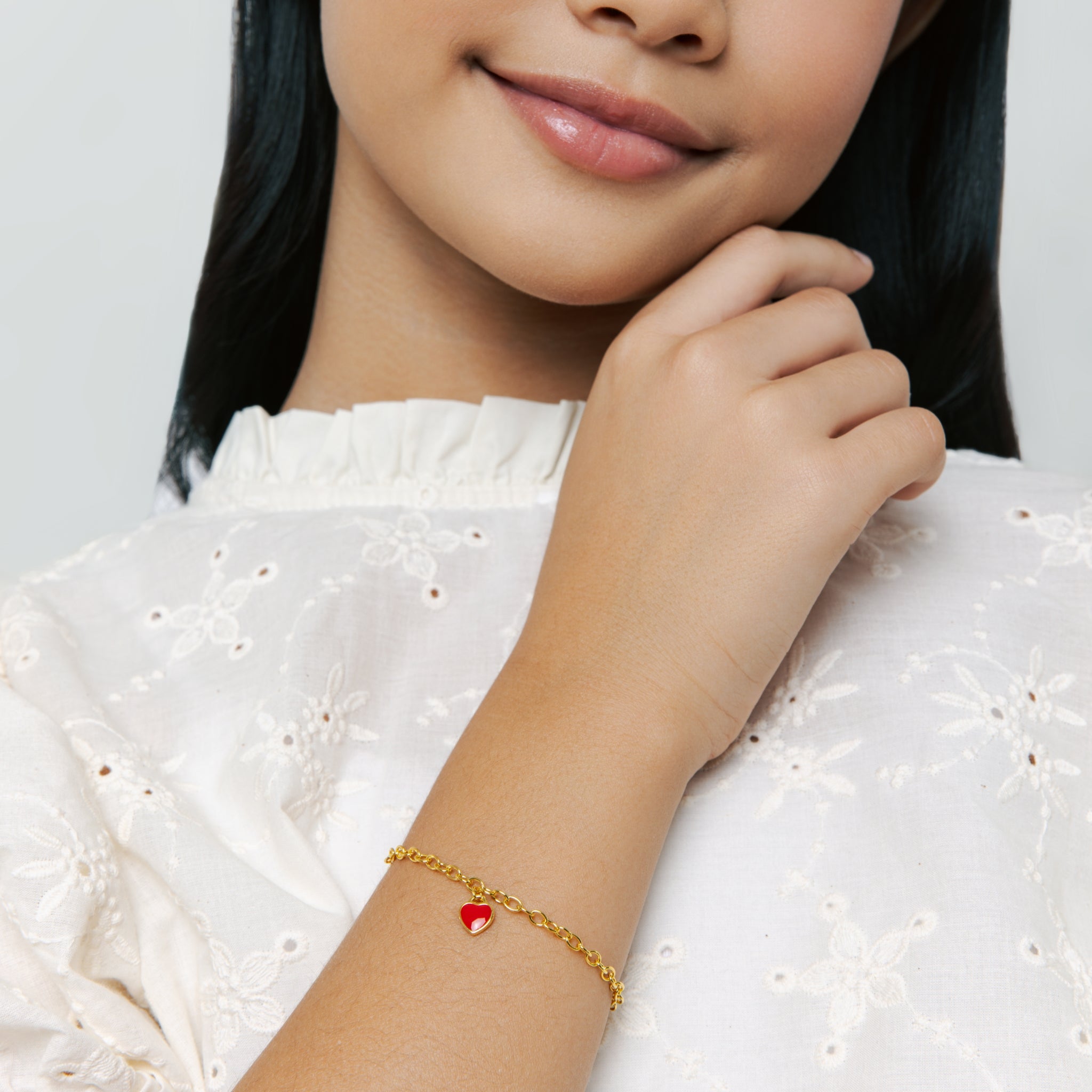 Model wears Red Central Heart Bracelet in vermeil with rolo chain and red enamel heart charm, styled as a charm cute bracelet, smiling on neutral background.
