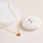 Flat lay of Ruby Liberty Stud Earrings and matching Ruby Liberty Necklace, both in vermeil with ruby corundum stones, on natural background for styling.