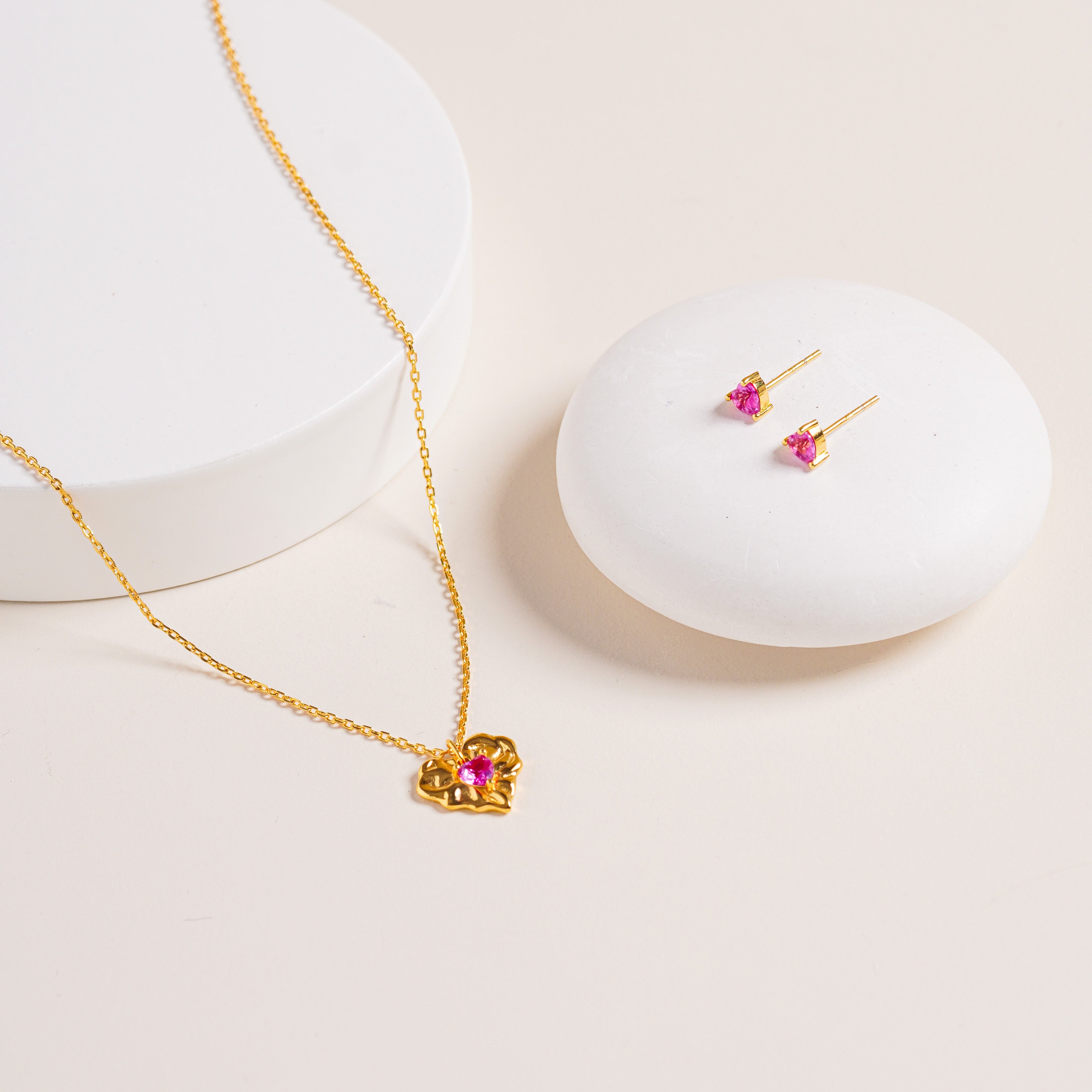 Flat lay of Ruby Liberty Stud Earrings and matching Ruby Liberty Necklace, both in vermeil with ruby corundum stones, on natural background for styling.