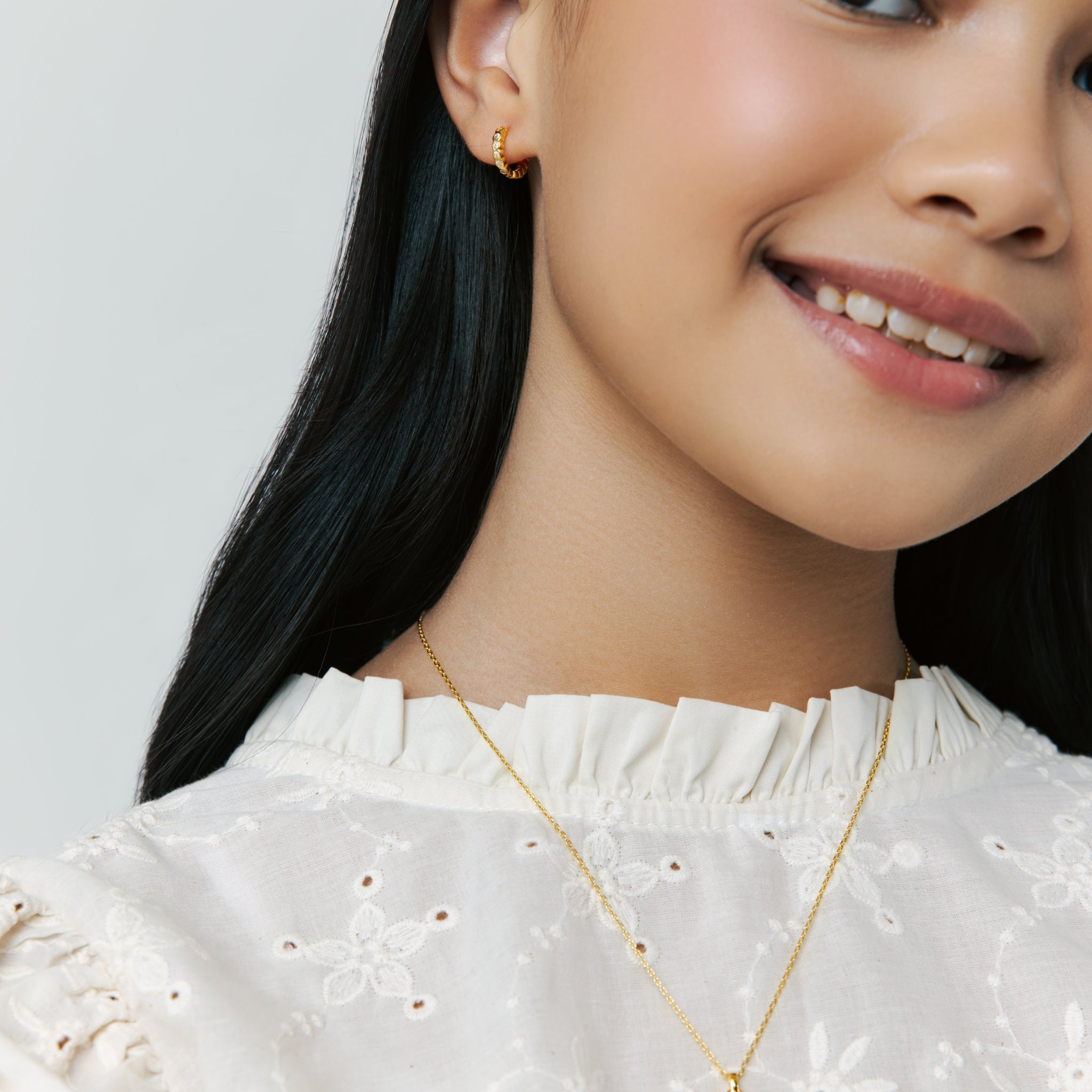 Model wears Twinkle Hoops earrings in vermeil with sparkling cubic zirconia, styled as small hoop earrings, smiling softly on neutral background.