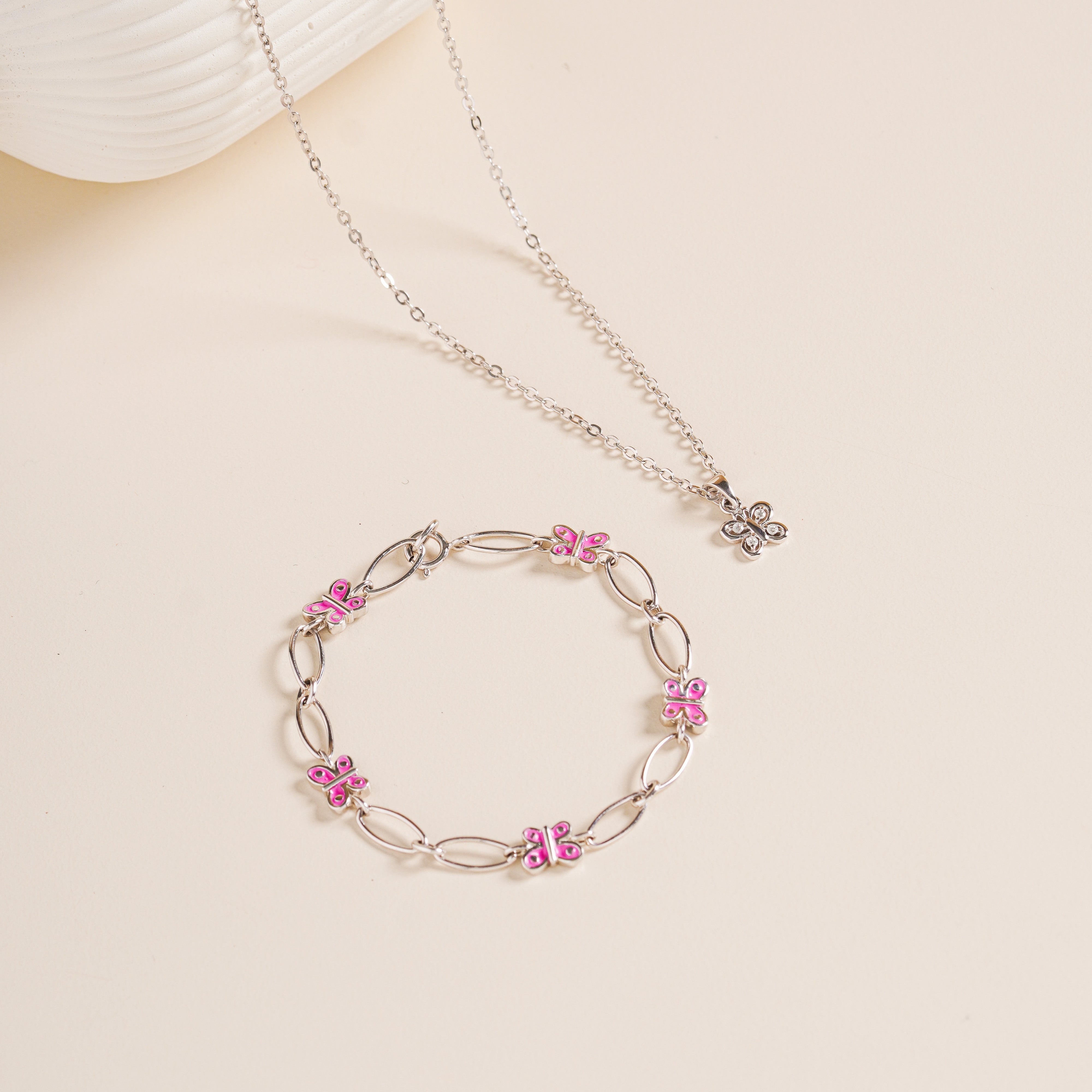 Flat lay of Brooklyn Butterfly Bracelet in pink enamel paired with matching necklace, sterling silver, on neutral background for display.